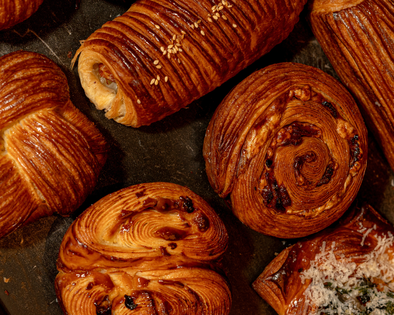 Close-up of various pastries including croissants and danishes on a dark surface.